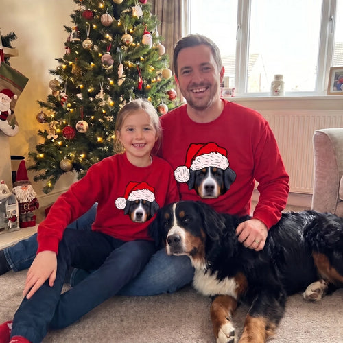 Dad and daughter in matching red novelty pet face Christmas sweatshirts with their Bernese mountain dog