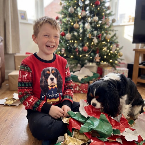 Boy on Christmas morning in a kids' premium pet face Christmas sweatshirt with his Cavalier in the wrapping paper