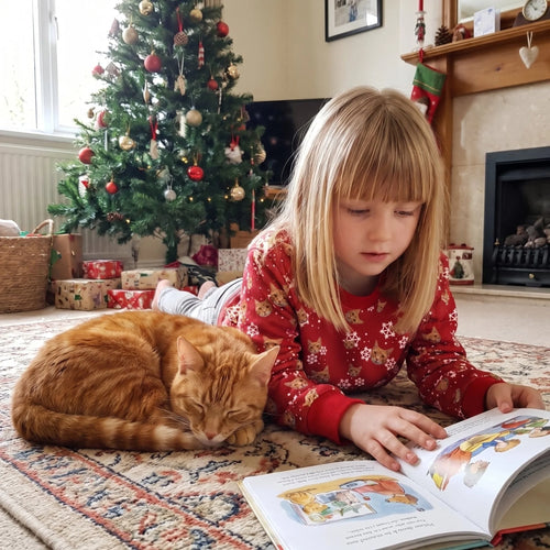 Girl reading by the Christmas tree in a kids' custom pet face pattern sweatshirt with her cat